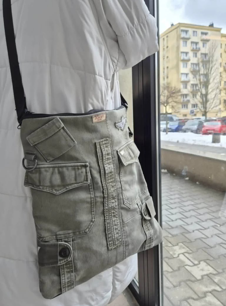 Person wearing white jacket and gray cargo pants with multiple pockets, standing indoors near a window overlooking a parking lot and apartment building