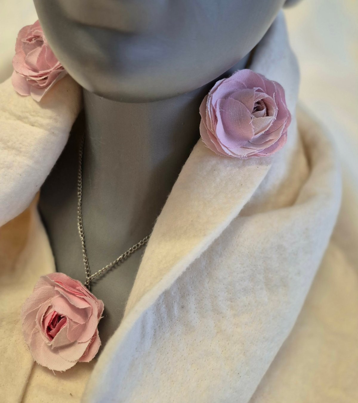 Mannequin wearing cream cardigan with pink roses adorning the neckline, shoulders, and a pendant necklace