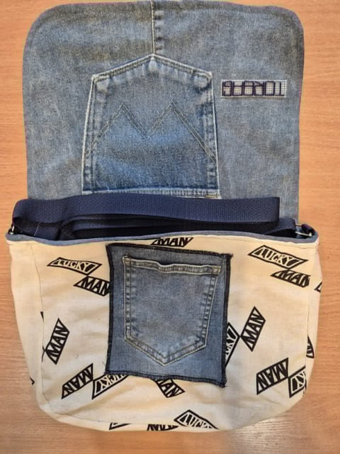 Two denim pouches with blue jeans pockets and a navy fabric handle, displayed on an orange surface