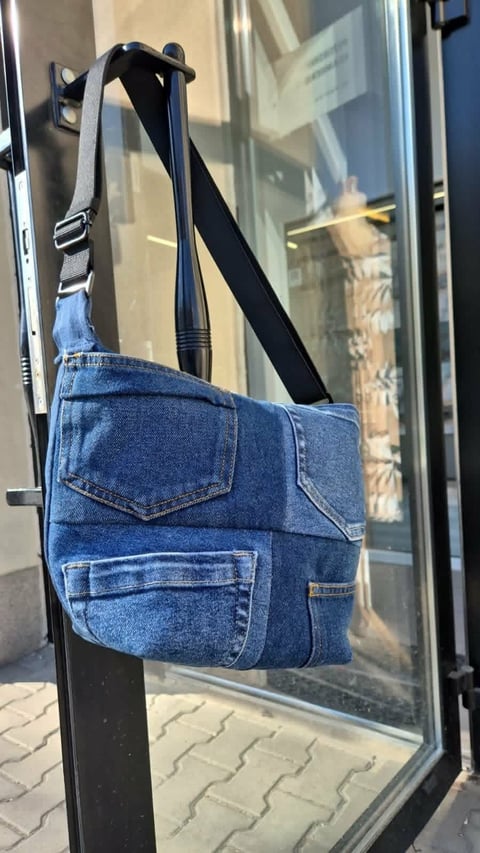 Blue denim bag with black strap hanging on display window of a storefront